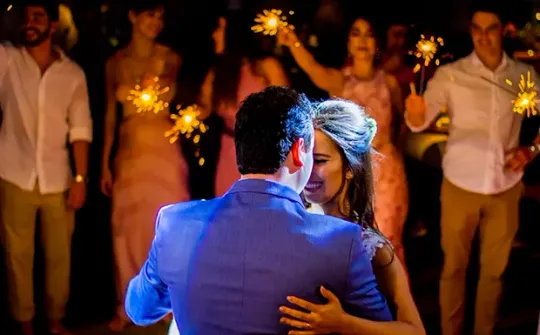 Uma noiva e um noivo estão dançando na recepção do casamento enquanto seguram estrelinhas.