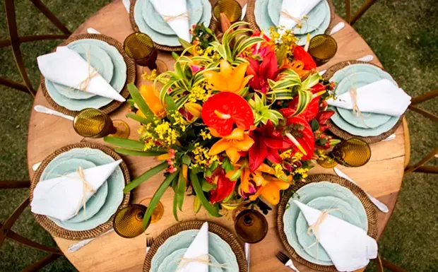 Uma mesa posta com pratos, guardanapos, copos e um buquê de flores.