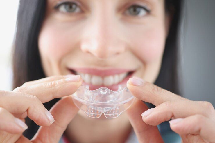 A woman is holding a clear retainer in front of her teeth.