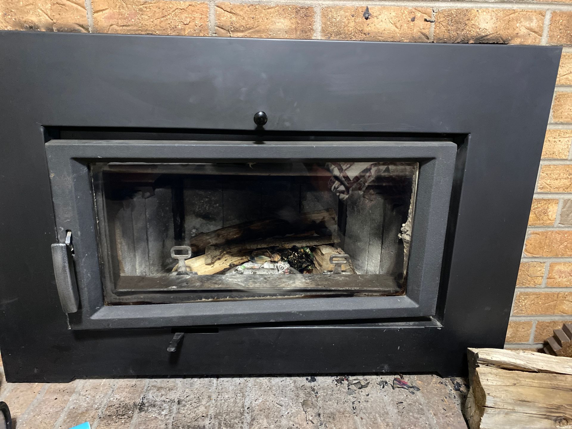 A fireplace with a door open and a brick wall behind it.