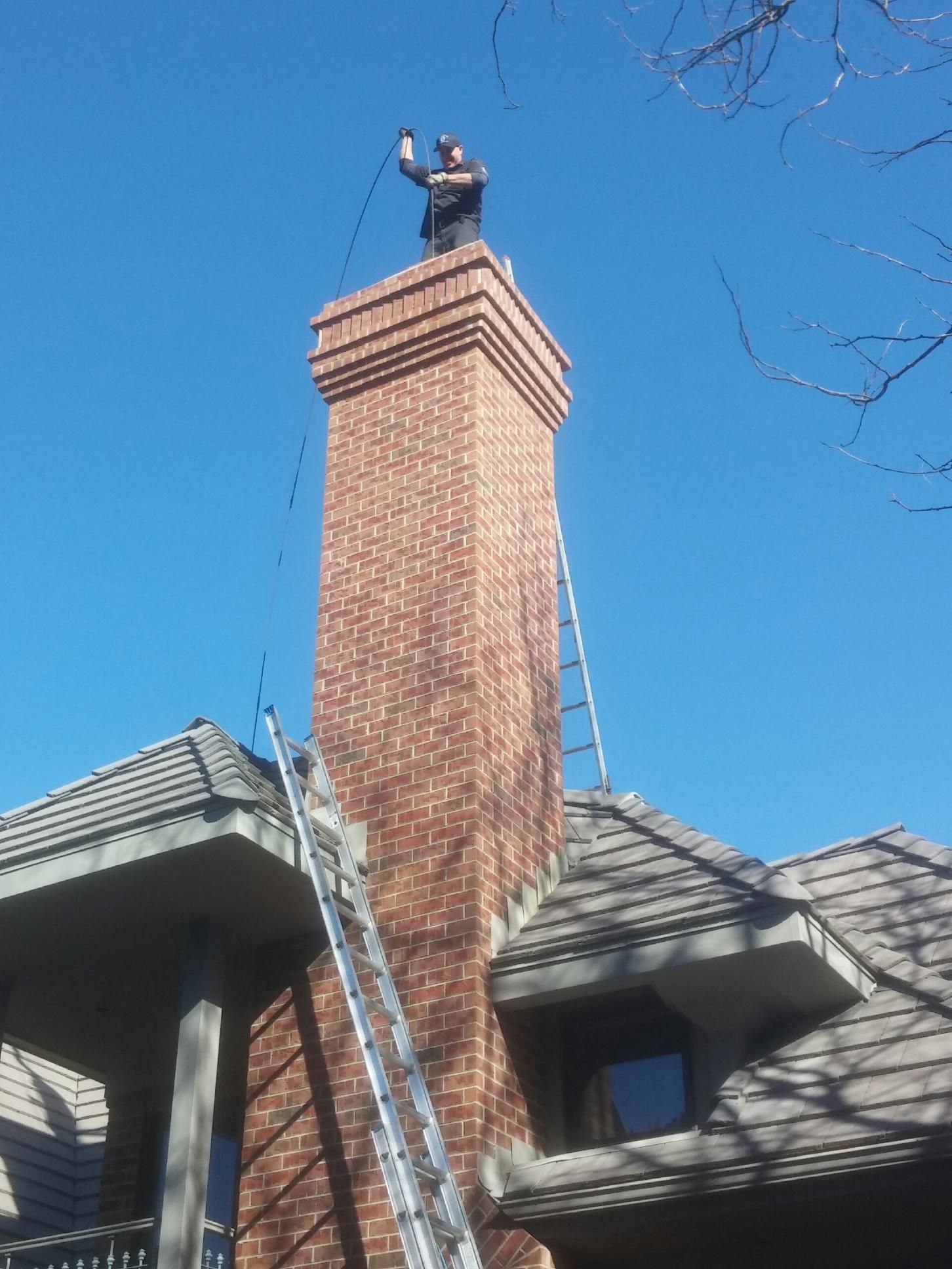 A man on top of a brick chimney with a ladder attached to it