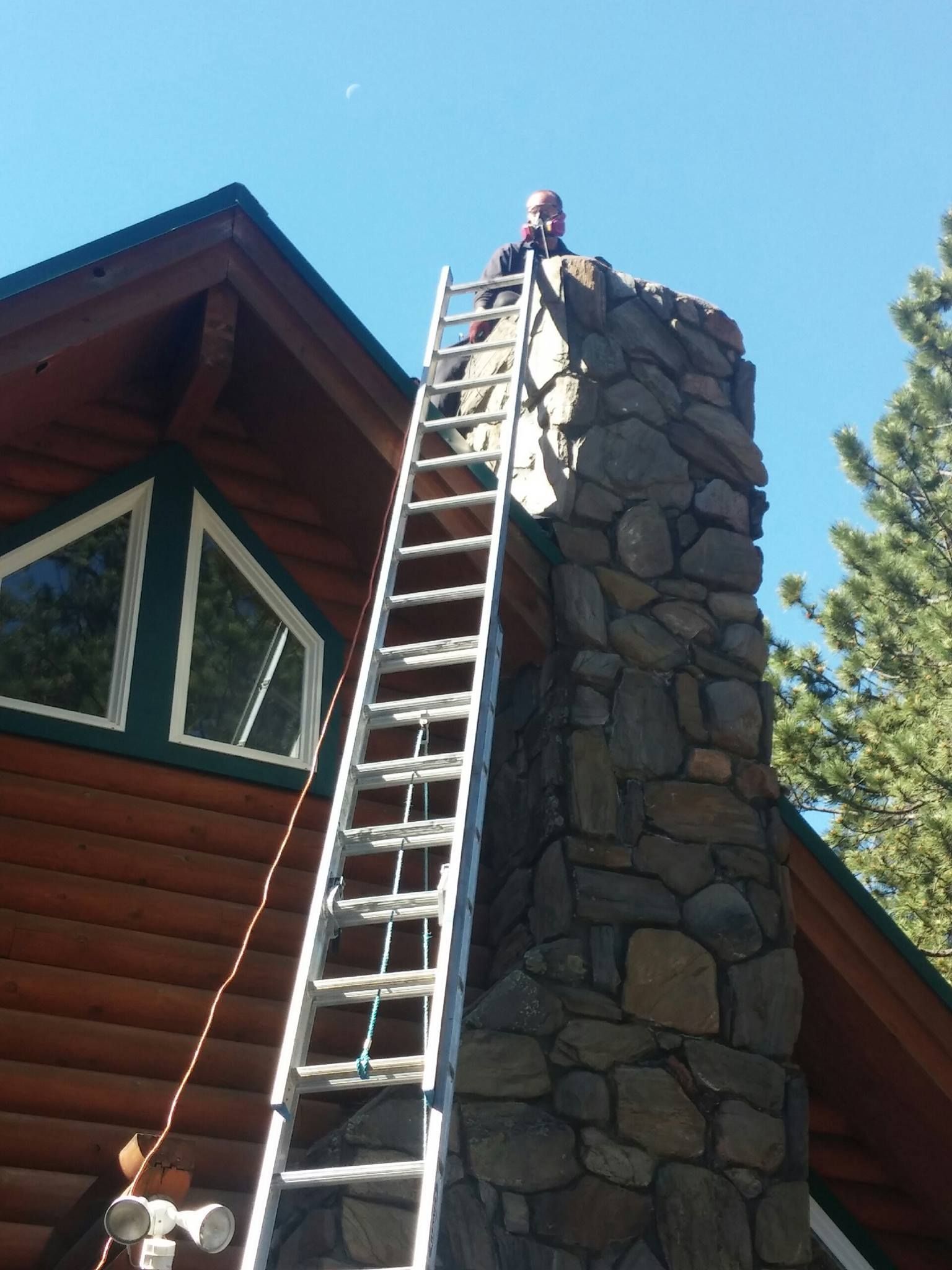 A man standing on top of a stone chimney with a ladder attached to it