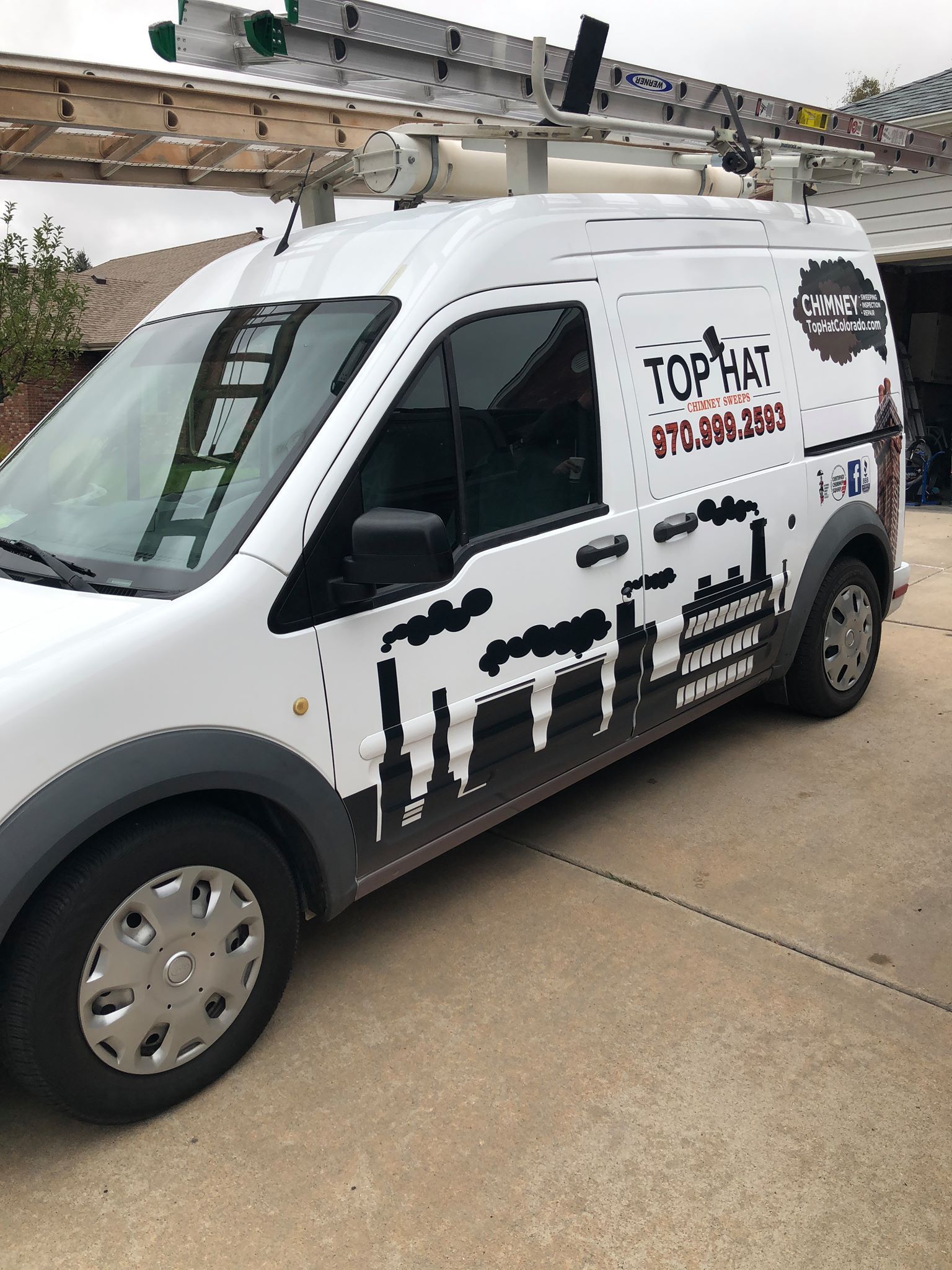 A white van with a ladder on top of it is parked in a driveway.
