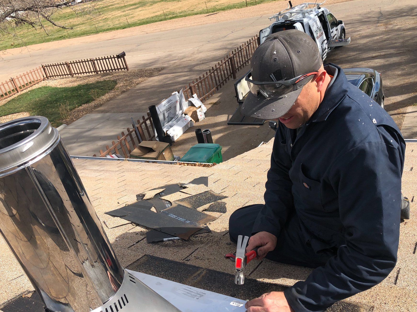 A man is kneeling on a roof working on a chimney.