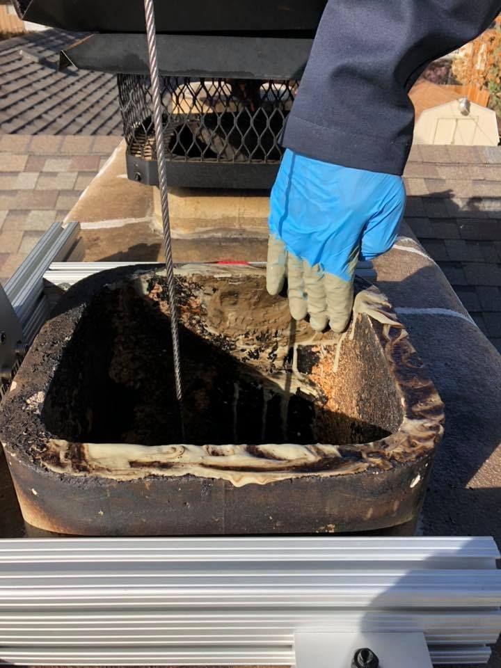 A person wearing blue gloves is holding a thermometer in a chimney.