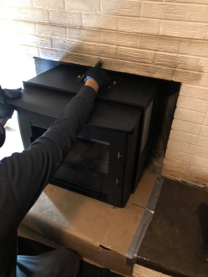 A man is installing a wood stove in a fireplace.