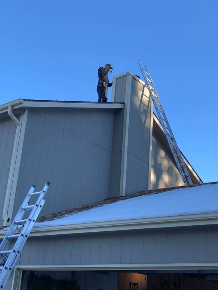 A man is standing on the roof of a house with a ladder.