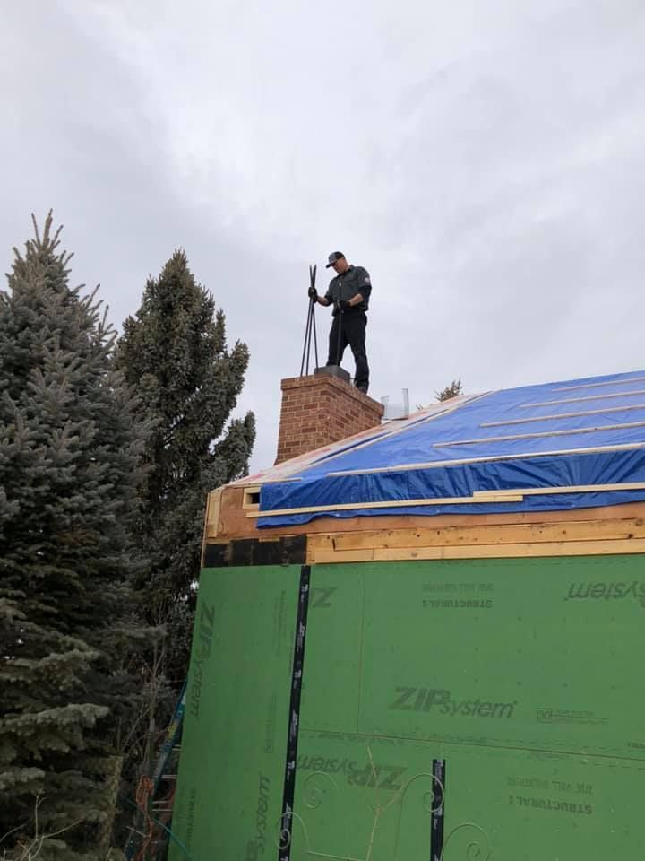 A man is standing on top of a roof with a chimney.