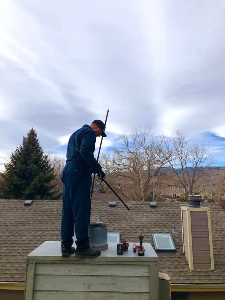A man is standing on top of a roof cleaning a chimney.
