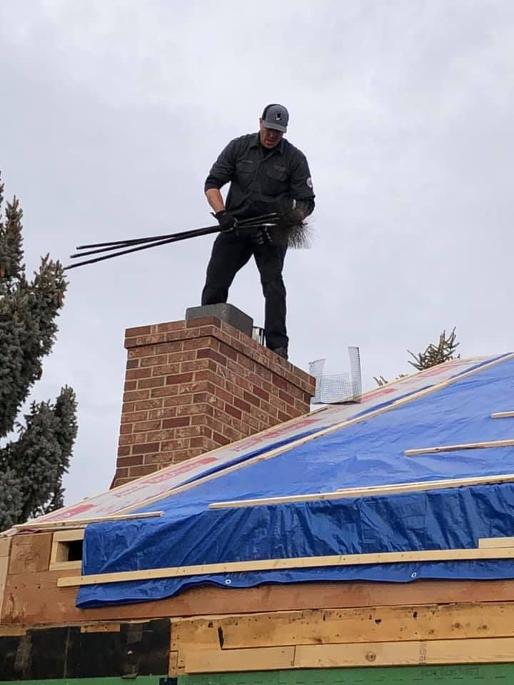 A man is standing on top of a brick chimney on a roof.