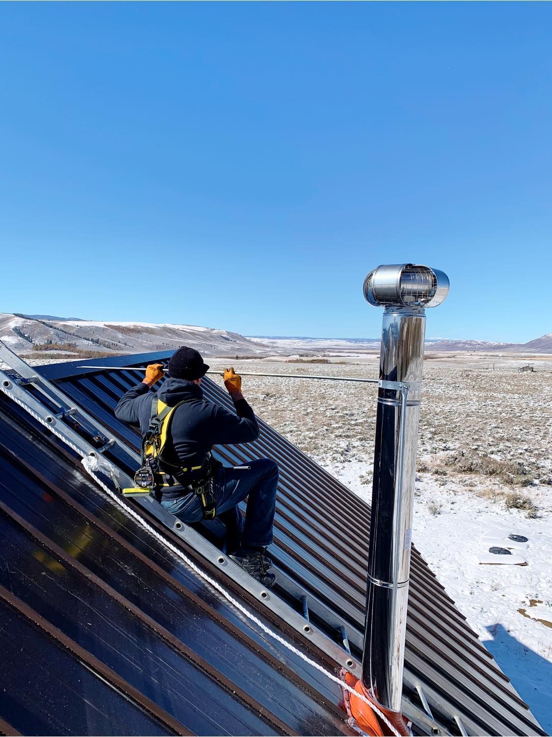A man is sitting on top of a roof installing solar panels.
