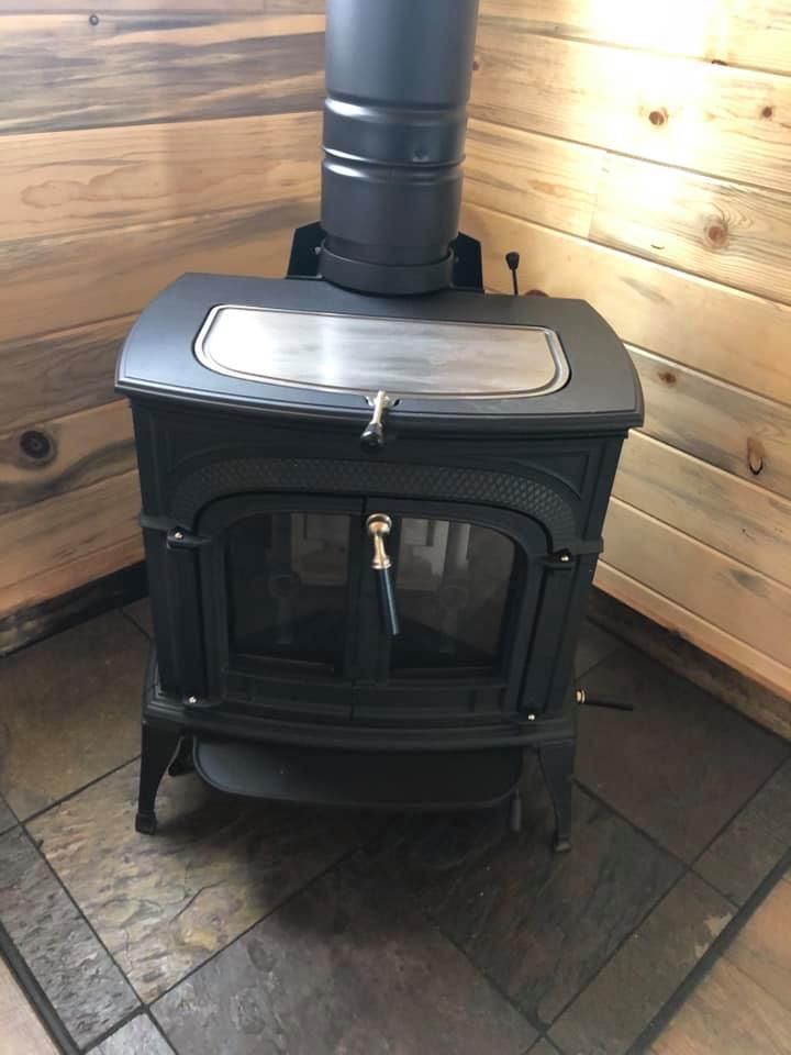 A wood stove is sitting in a corner of a room next to a wooden wall.