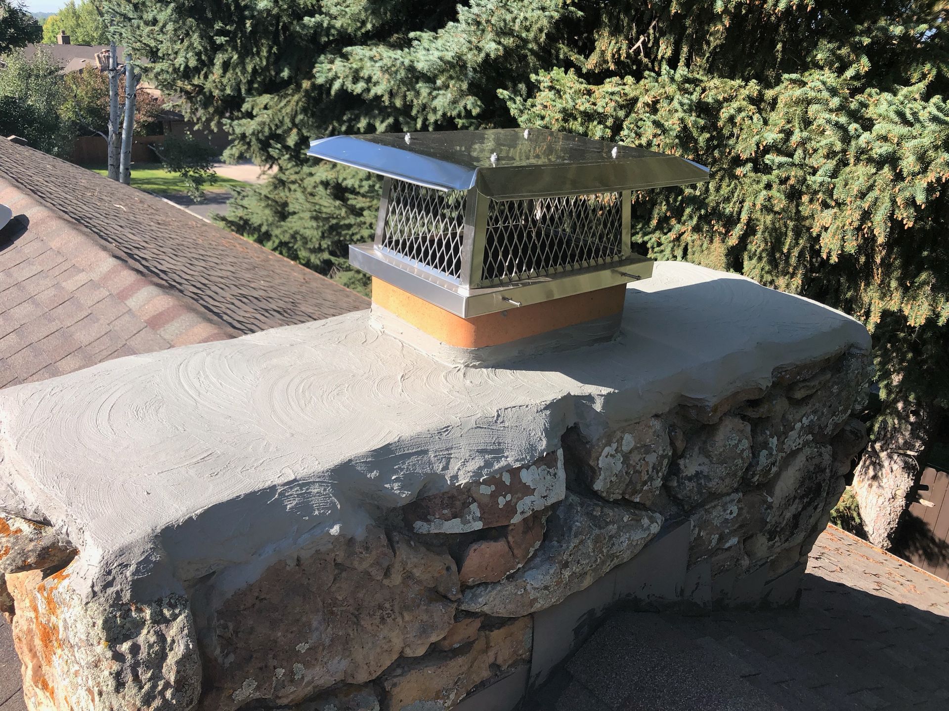A chimney on top of a stone wall with trees in the background