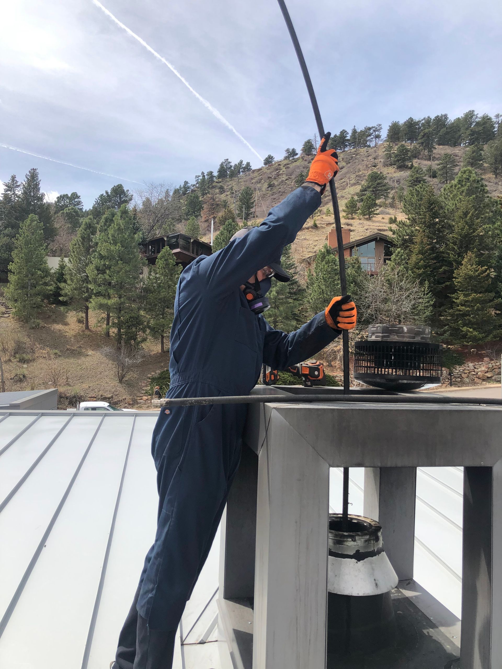 A man in a blue jumpsuit is cleaning a chimney on top of a building