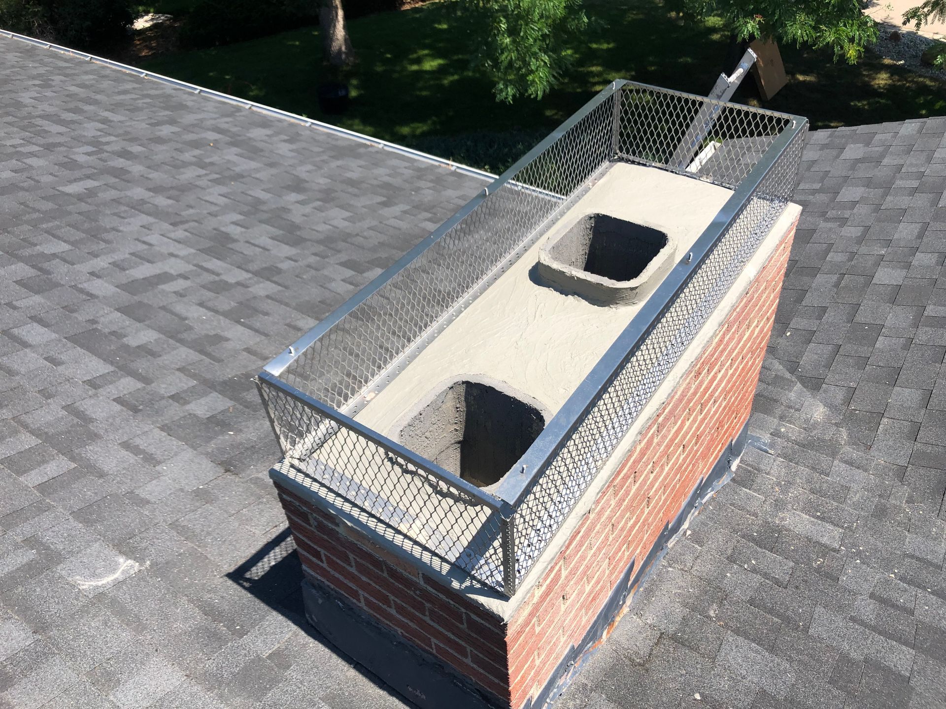 A brick chimney on top of a roof with a metal fence around it