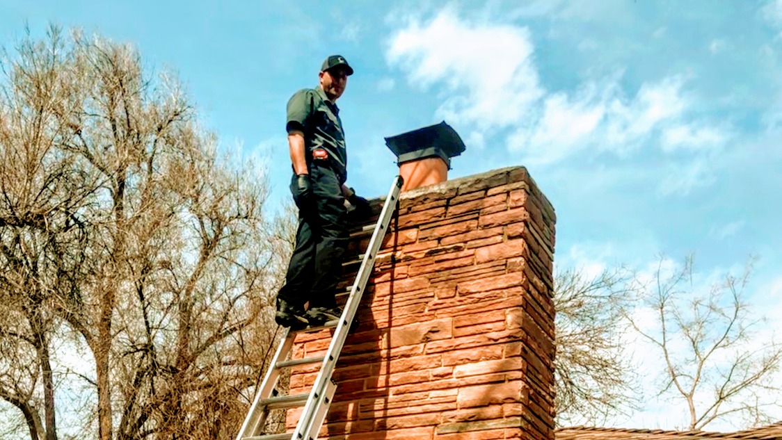 A man is standing on a ladder on top of a brick chimney.