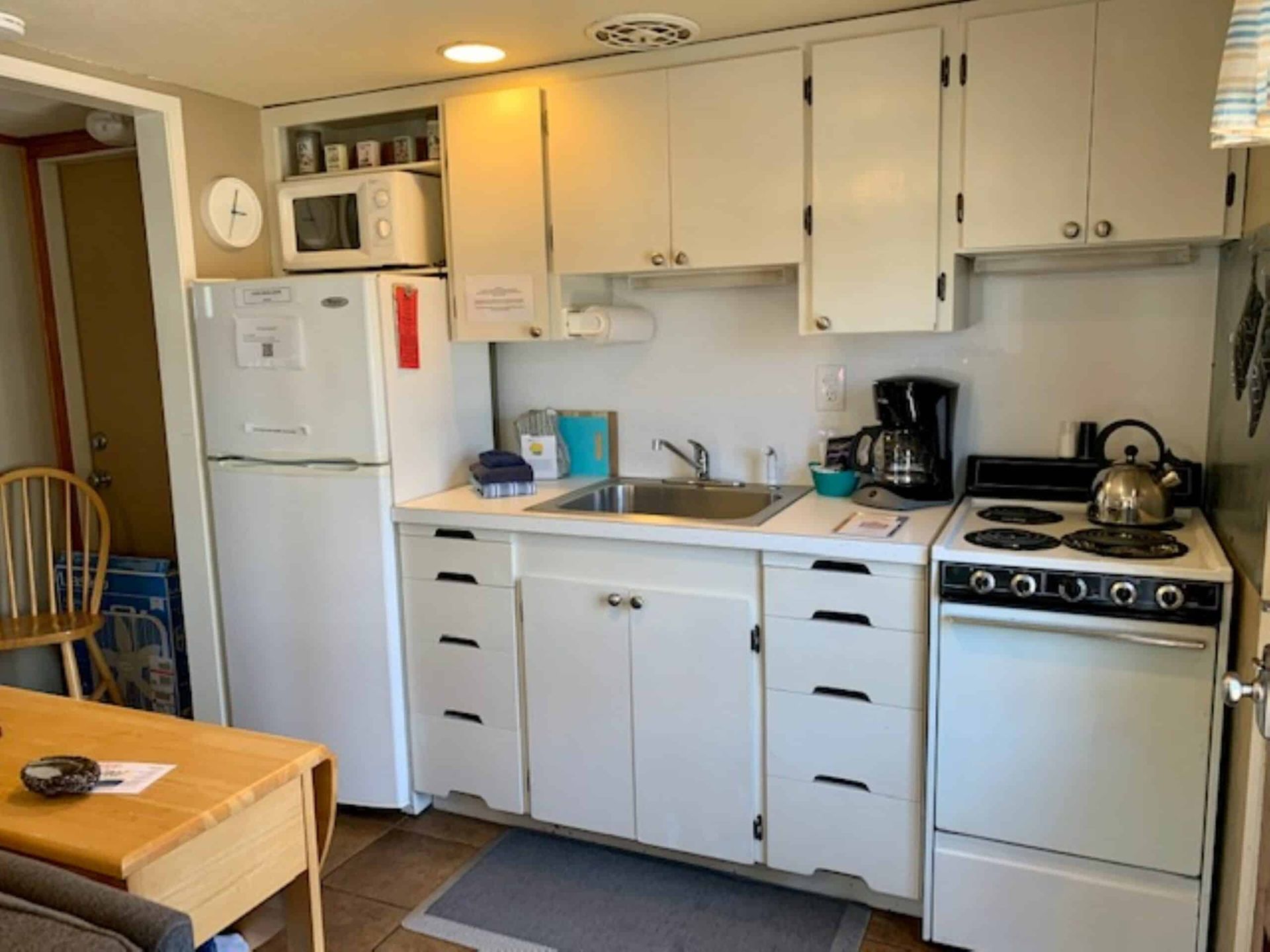 A small kitchen with white cabinets , a stove , refrigerator , sink and microwave.