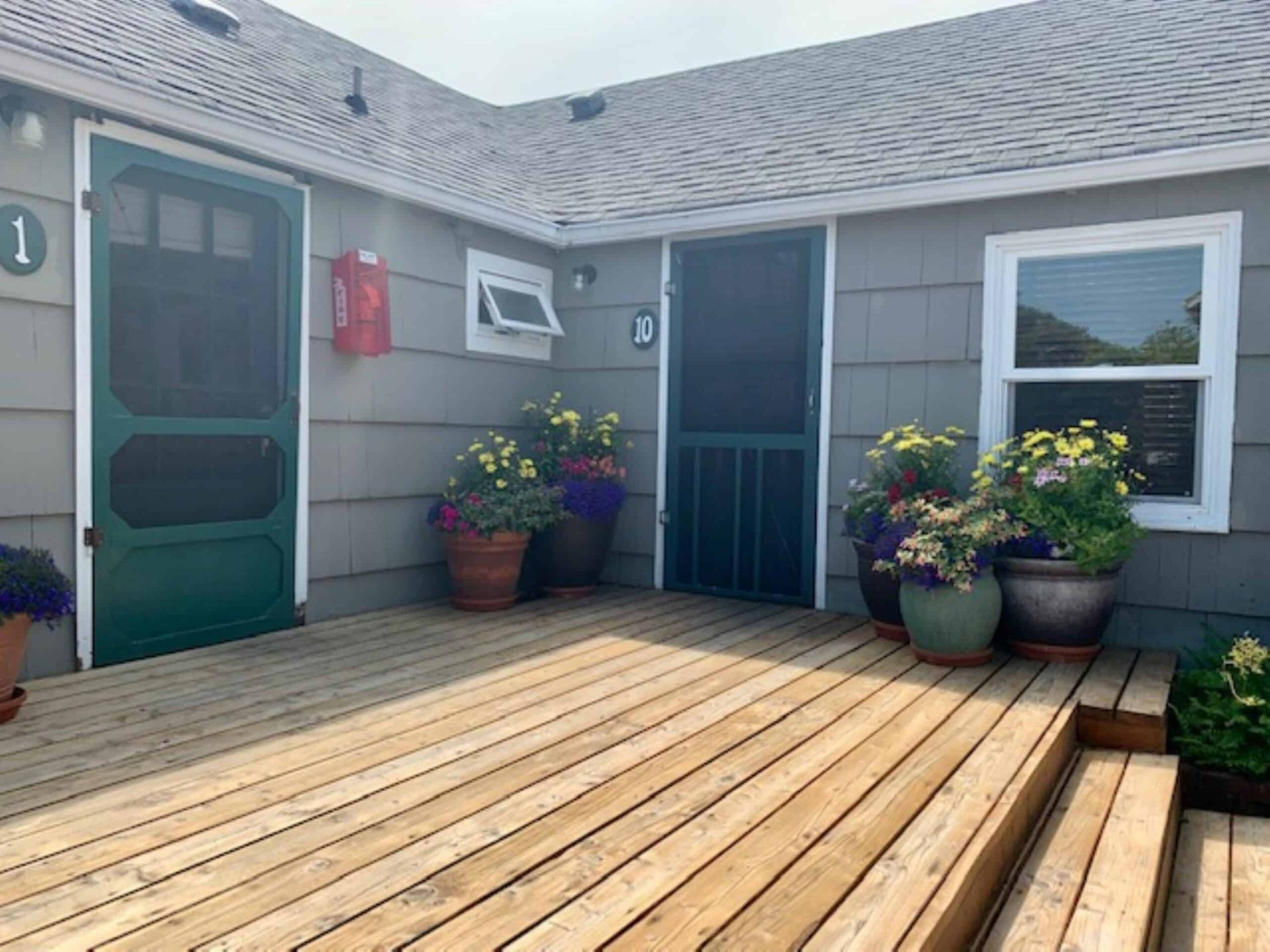 A house with a wooden deck and potted plants in front of it.