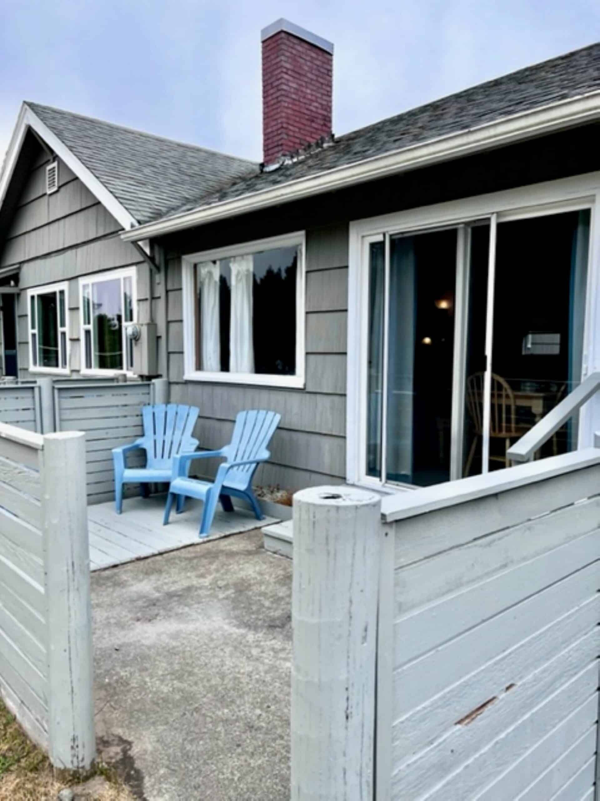 Two blue chairs are sitting on a patio in front of a house.