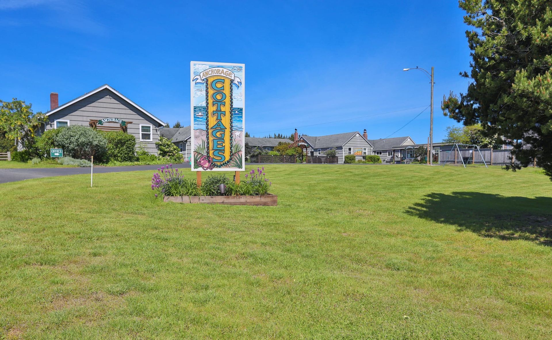 A tall, colorful sign in a grassy area with houses and a blue sky in the background.