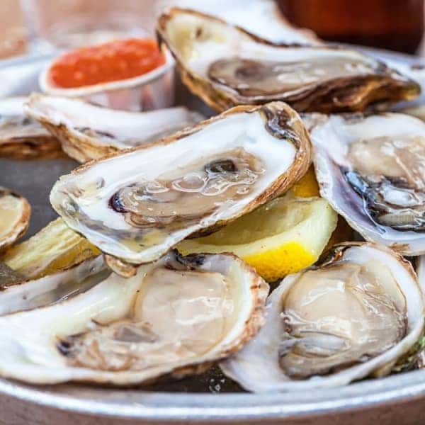A plate of oysters with lemon slices and sauce on a table.