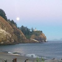 A beach with a lighthouse in the distance and a full moon in the sky.