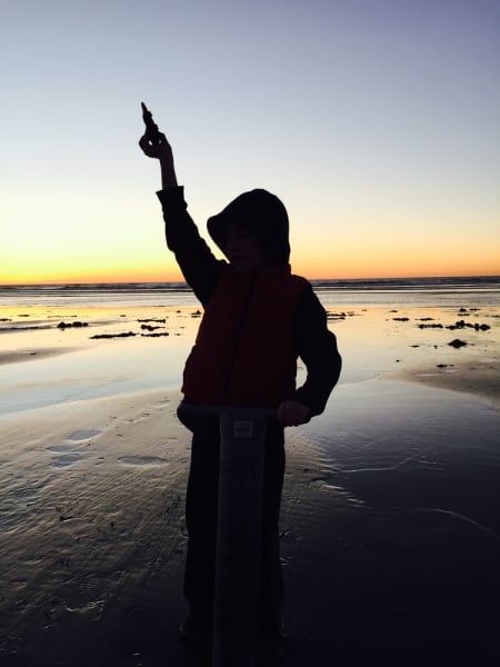 A person standing on a beach pointing at the sky