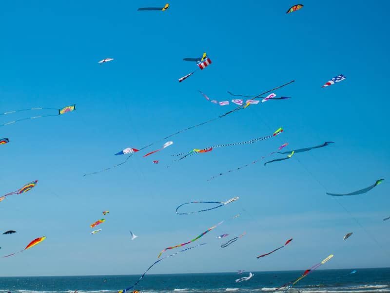 A bunch of kites are flying in the sky over the ocean.