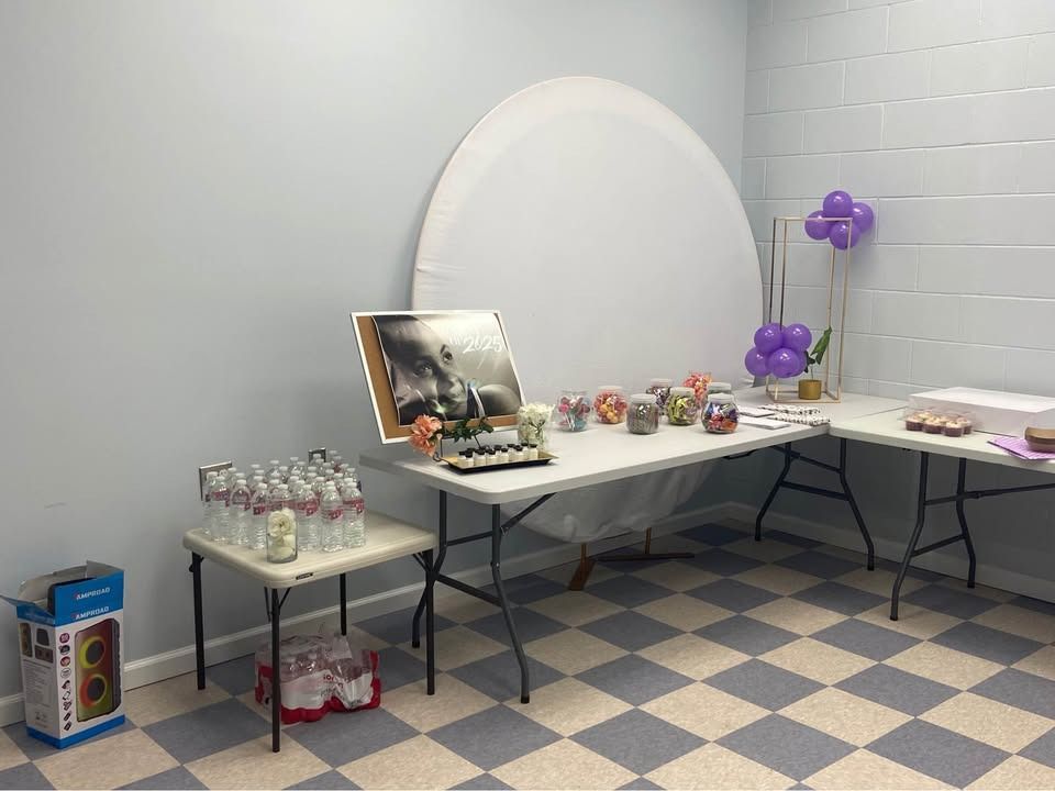 Party setup with tables, snacks, drinks, balloons, and artwork against a light blue wall in a room with a checkered floor.