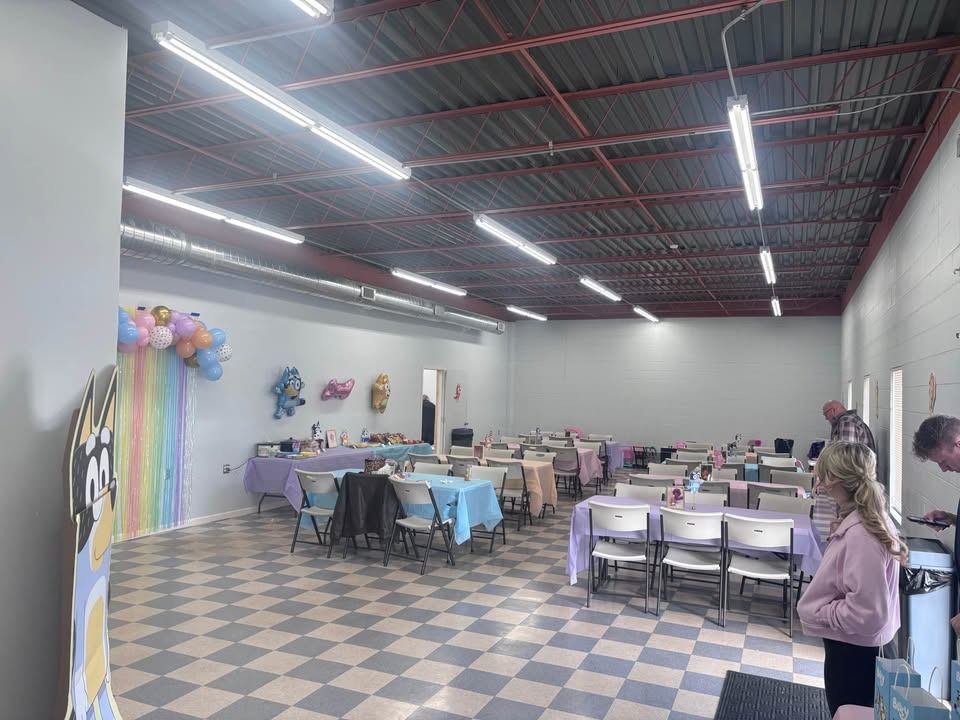 Party room set up for an event, tables with colorful linens, decorations on the walls, checkered floor, people present.