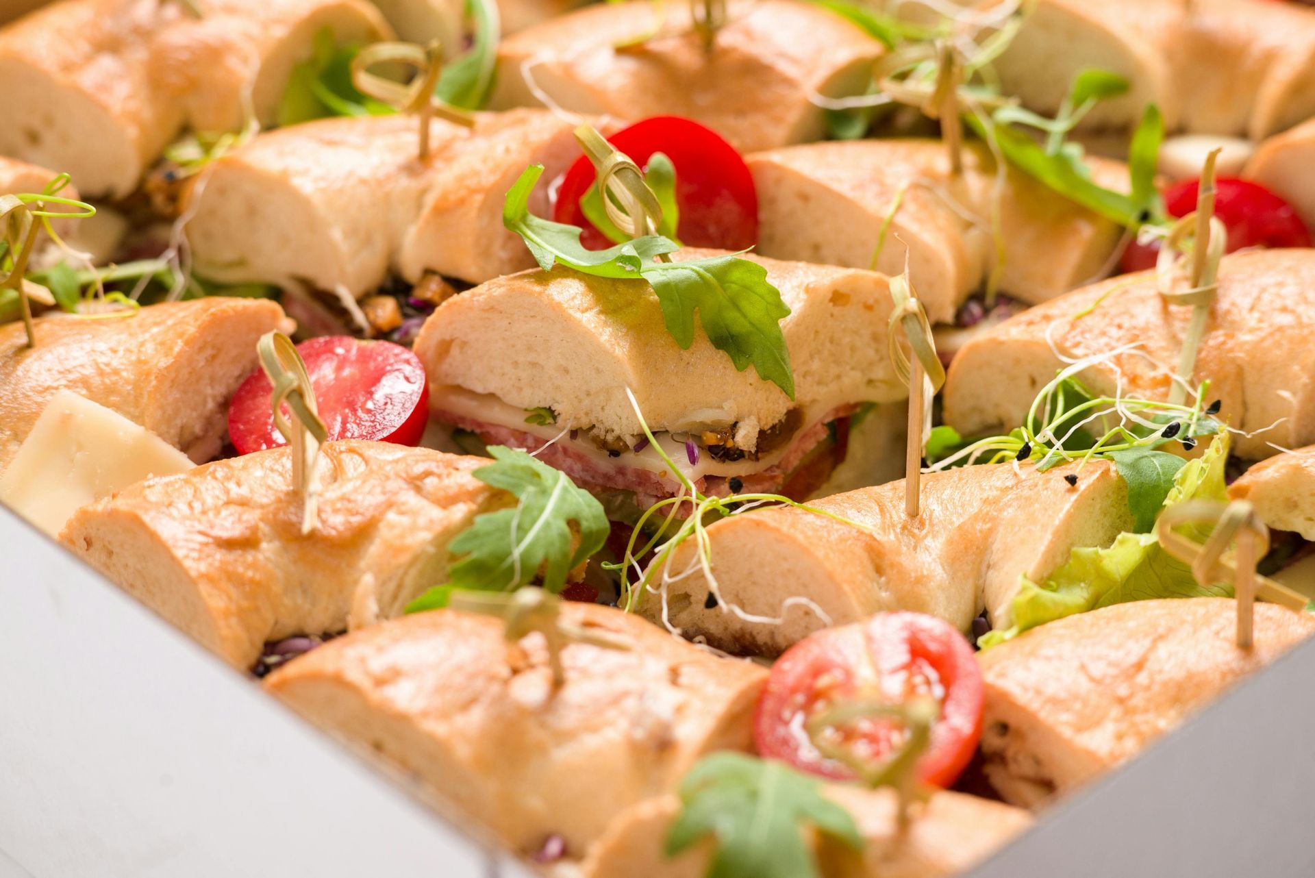 Sandwich platter with baguette sandwiches, cherry tomatoes, and greens.