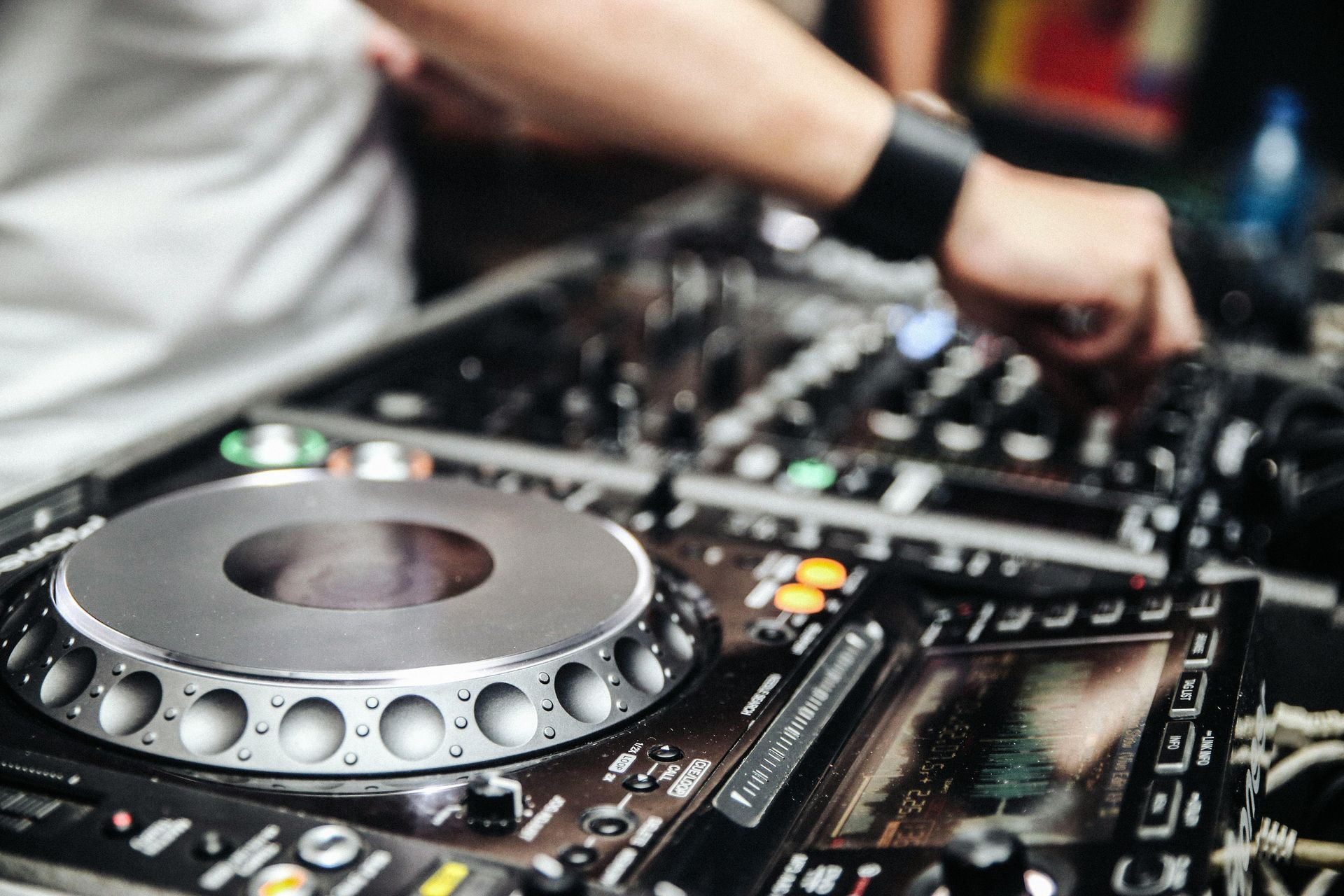 DJ at work, hand adjusting mixing console. Silver turntable, black equipment.