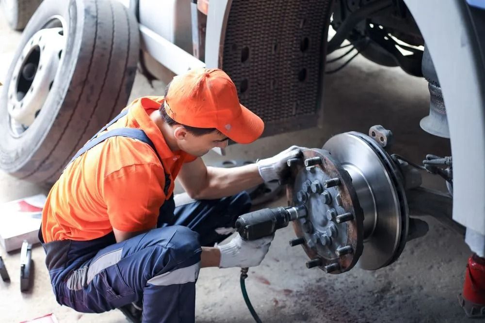 A Mechanic in an Orange Uniform Uses an Impact Wrench to Repair the Brake — B & W Commercials In Wauchope, NSW