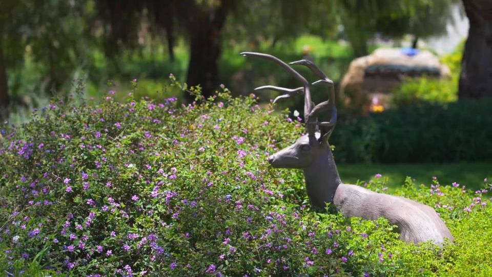 a statue of a deer laying in the grass surrounded by purple flowers .