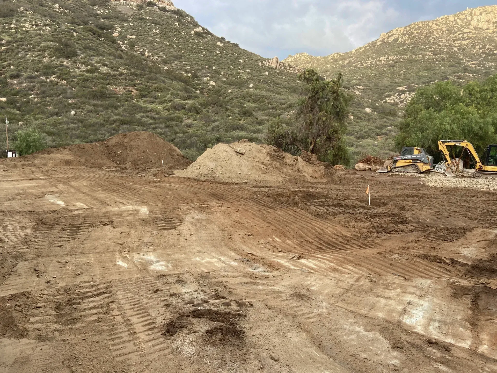 Construction site, dirt piles, and equipment in front of a mountain.