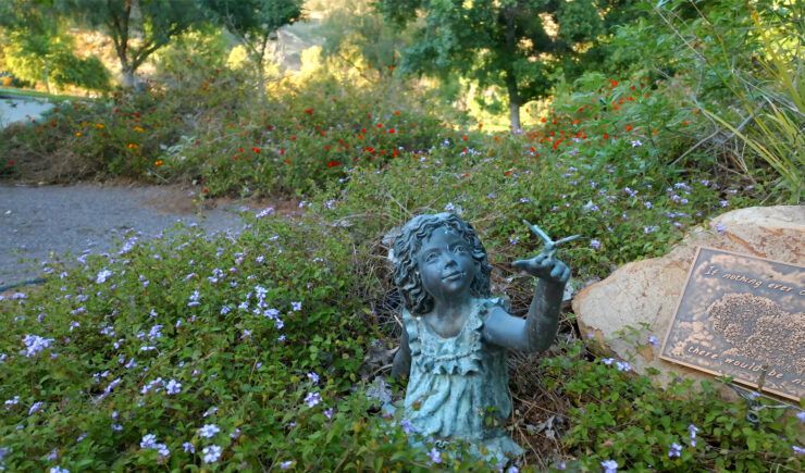 a statue of a girl holding a flower in a garden .