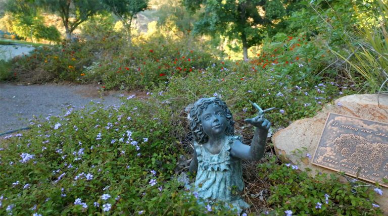 a statue of a little girl holding a flower in a garden .
