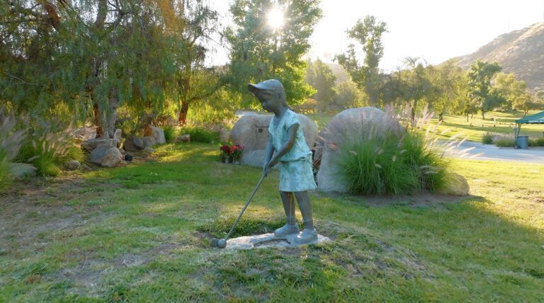 a statue of a boy holding a golf club in a park .