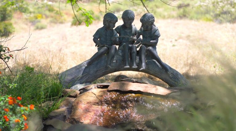 a statue of three children sitting on a bridge over a stream .