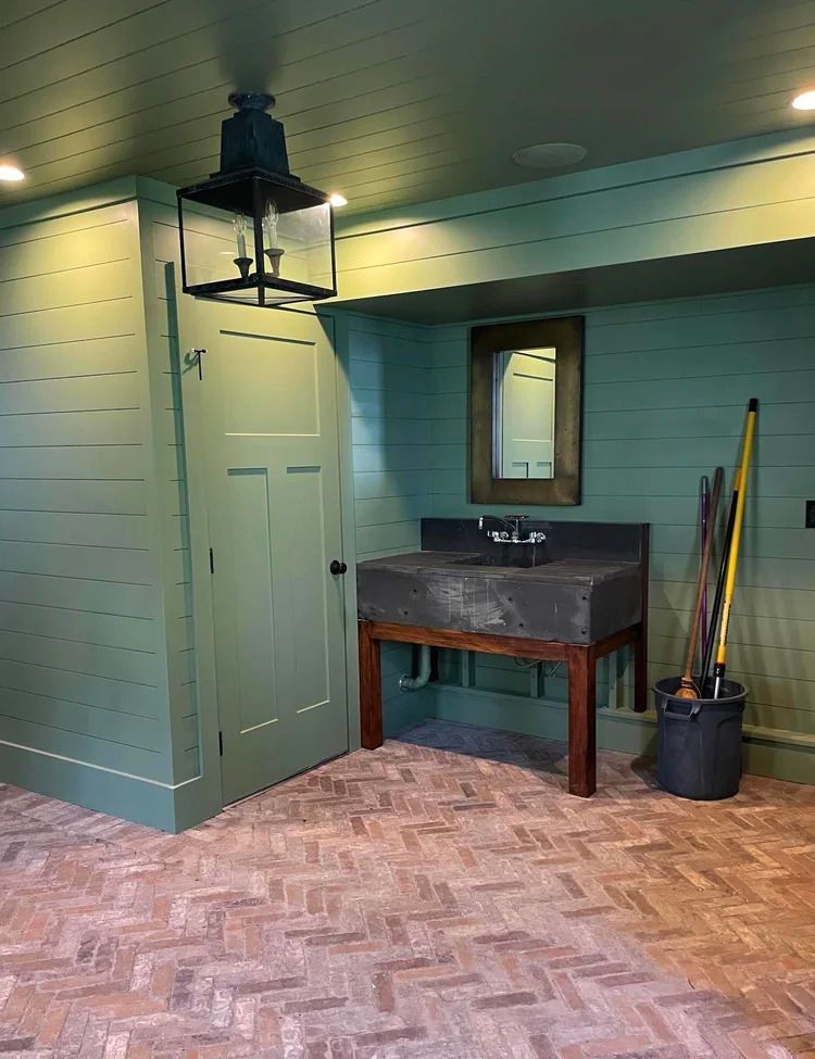 Green-painted room with brick floor, a sink, and a door, beneath a lantern fixture.
