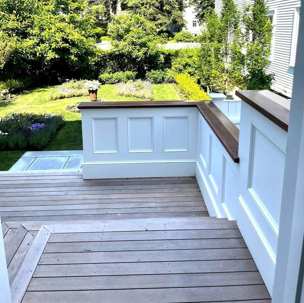 Wooden deck and stairs leading down to a garden with white railing and trees in the background.