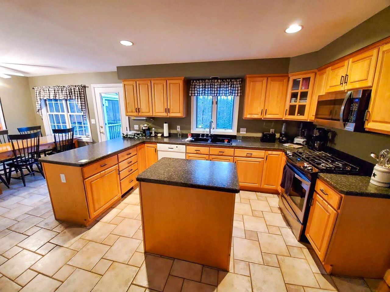 A kitchen with light wood cabinets, dark countertops, a center island, and tiled floor.