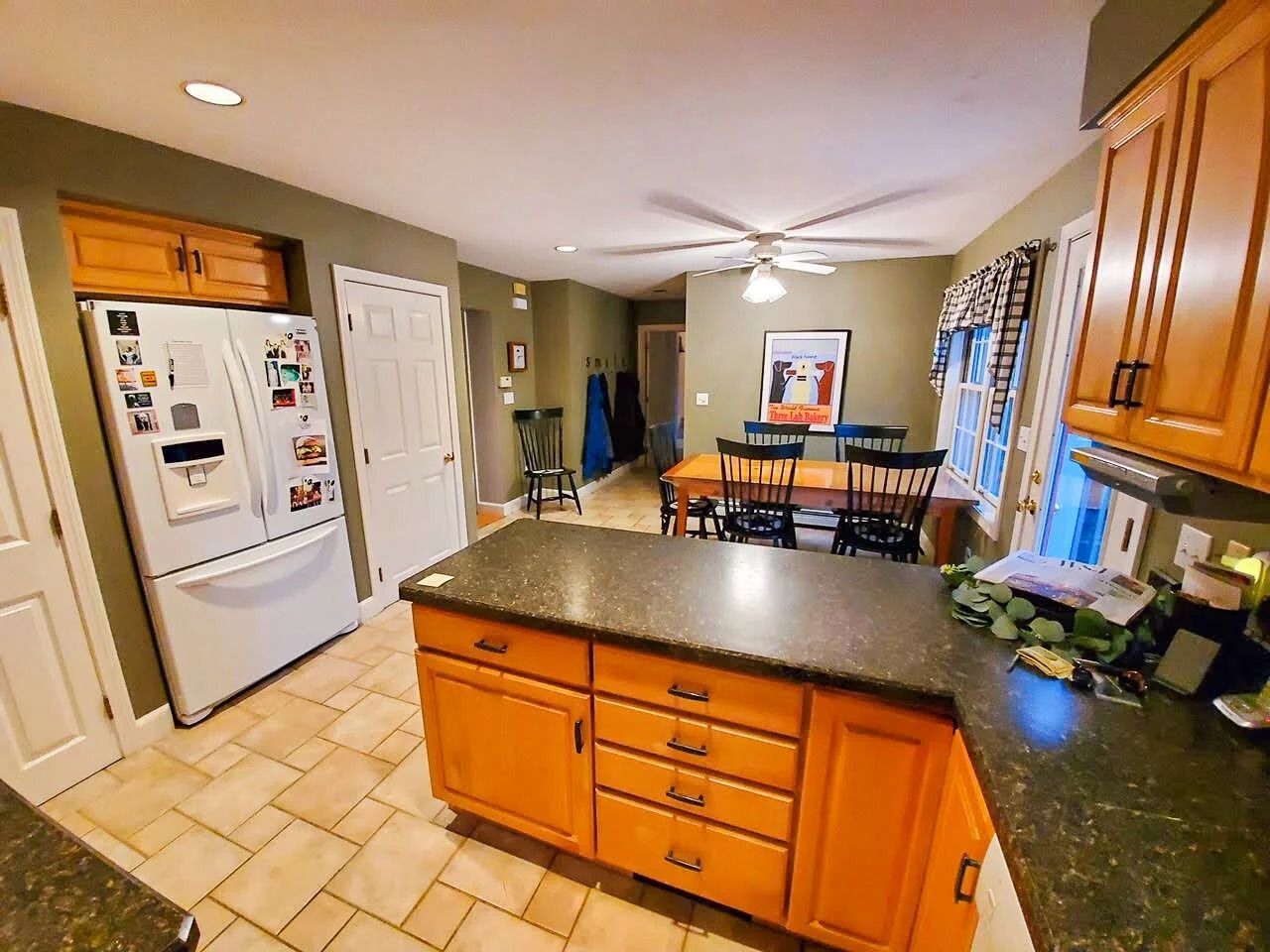 Kitchen with orange cabinets, granite countertops, tile floor, refrigerator, and dining area.