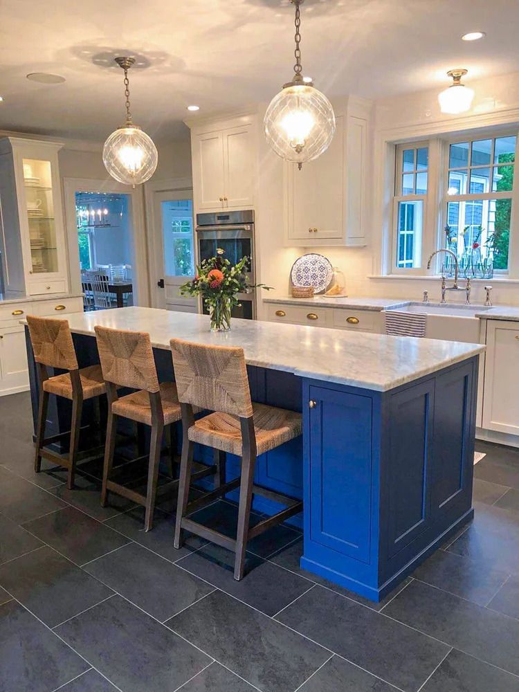 Blue and white kitchen with island, marble countertop, pendant lights, and woven bar stools.
