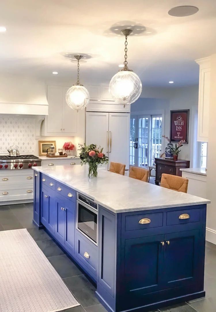 Blue kitchen island with marble countertop, pendant lights, and built-in microwave.