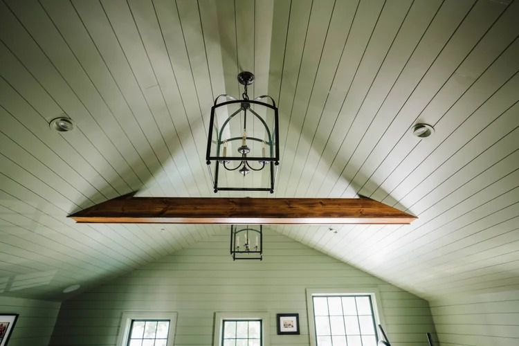 Light green, slatted ceiling with a dark metal chandelier and brown wooden beam.
