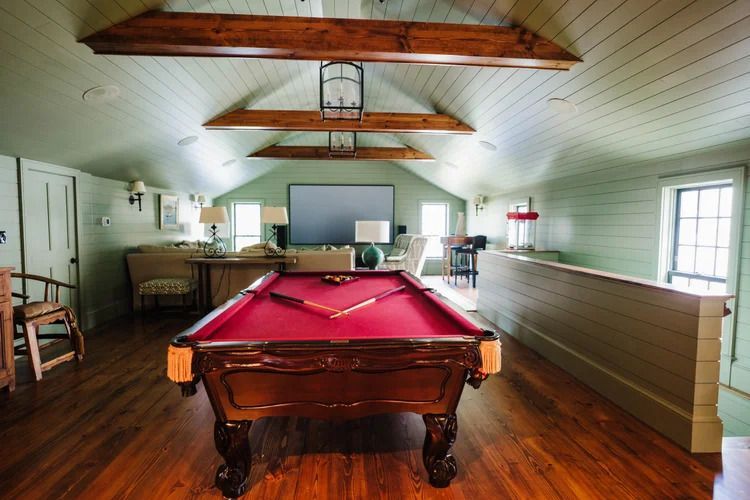 Pool table in a game room with red felt and wood trim, next to a seating area.