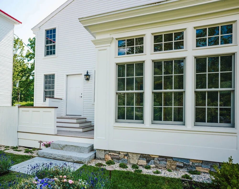 White house with large windows, stone steps, and a flower bed. Historical District Home in Kennebunk, Maine
