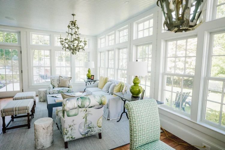 Bright sunroom with white trim, large windows, floral and green furniture, and chandelier.