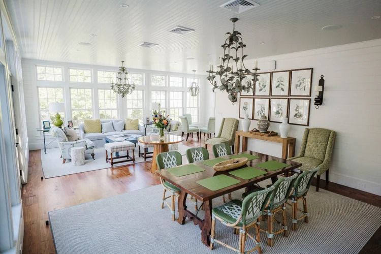 Sunlit dining room and living space with chandelier, wood table, and green chairs.